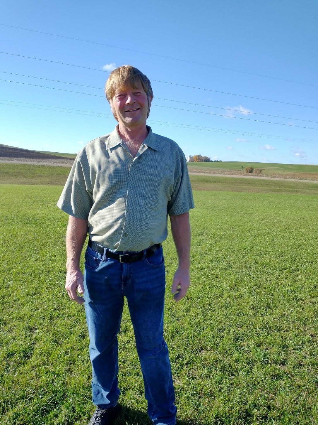 Mike Orbeck smiling and standing in a grass field. 