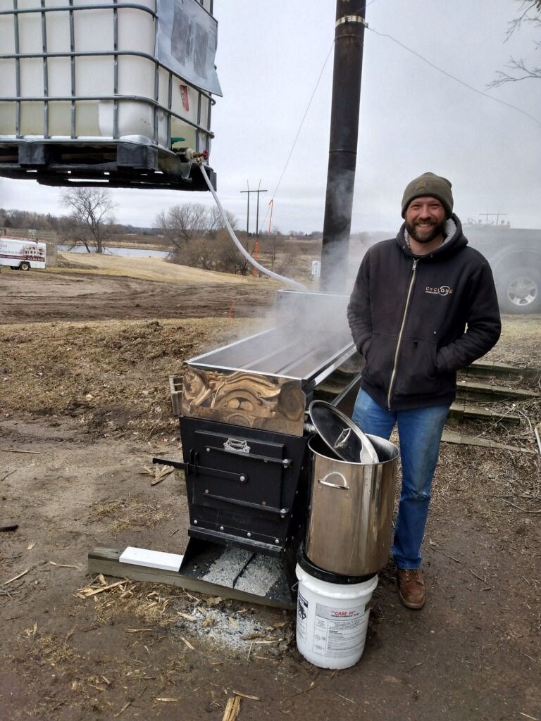 Mike Seifert smiling and standing next to a maple sap evaporator emitting steam.