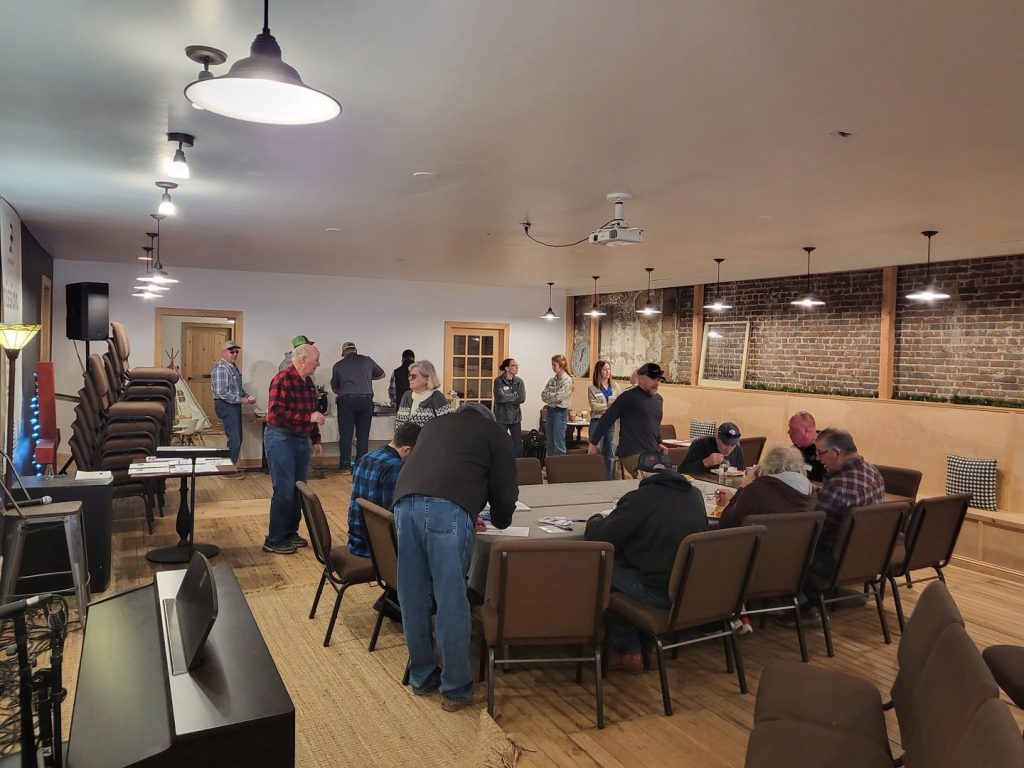 Farmers sitting at a table and eating lunch, and others gathered around the room in conversation with each other. 